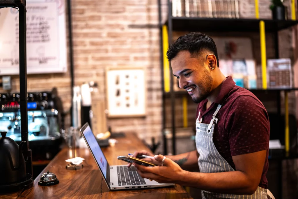 Small business owner young man using laptop and talking on mobile phone at a coffee shop