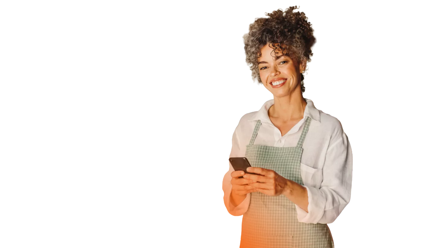 Successful female cafe owner using a smartphone in her cafe. Mature business owner smiling at the camera while standing in front of the counter. Businesswoman sending a text message.